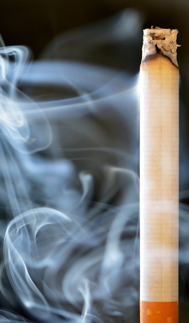 A lit cigarette with smoke rising up towards the top of the image.