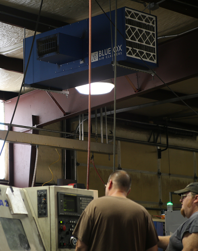 Machine operators working while a Blue Ox air filtration system cleans and circulates air above them.
