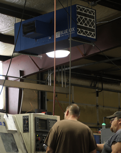 Machine operators working while a Blue Ox air filtration system cleans and circulates air above them.