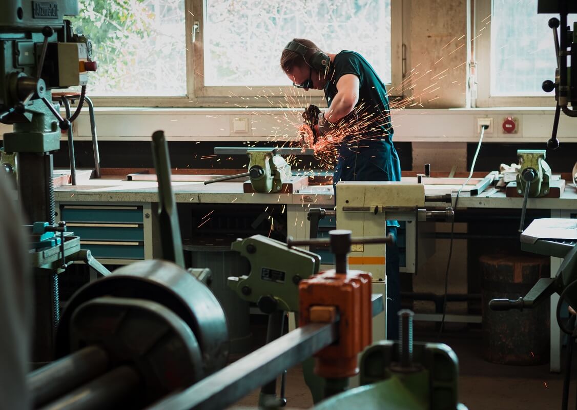 A welder working on a project while sparks emit, surrounded by various types of welding equipment and machinery.