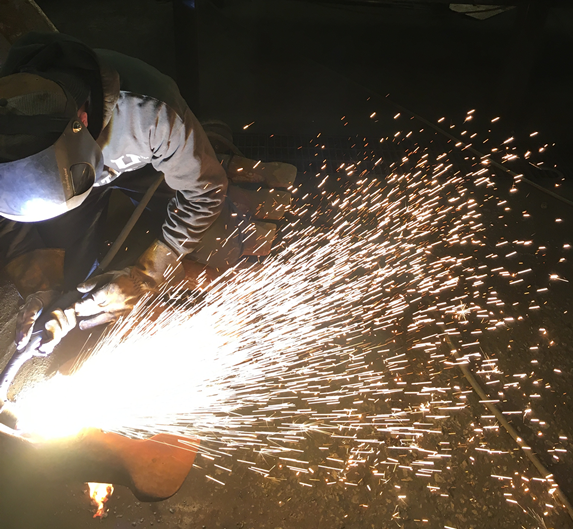Machine operator at AIS Construction working on a welding project while sparks emitted.